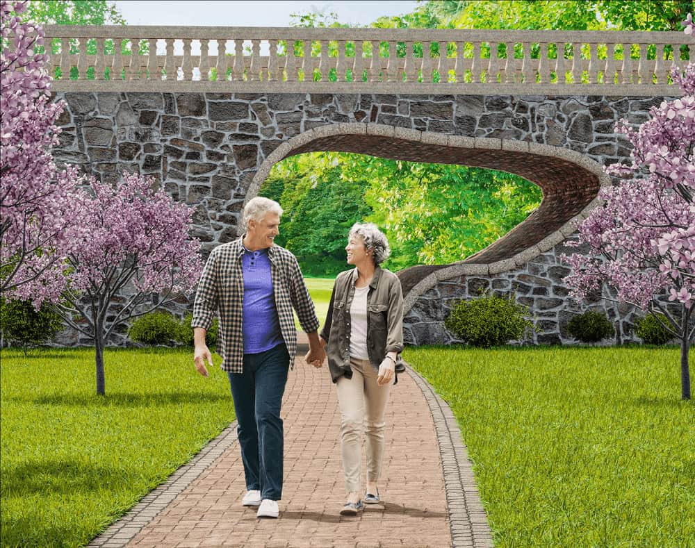 Older couple walking together on a park path beneath a stone bridge surrounded by flowering trees